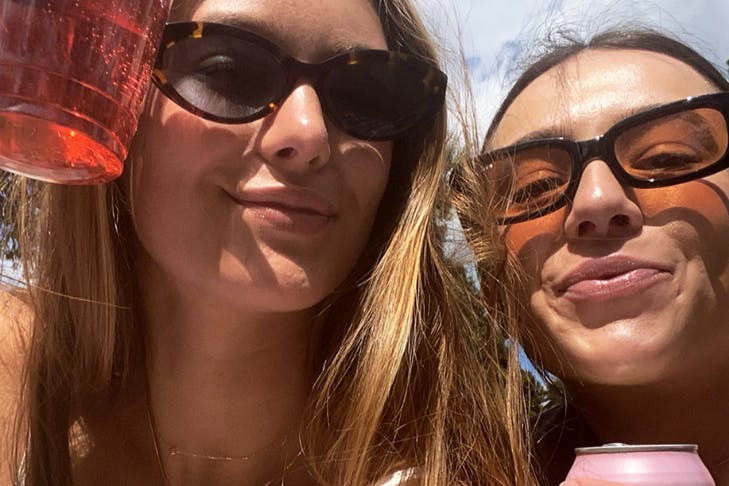 Two girls with drinks in their hands looking at the camera.